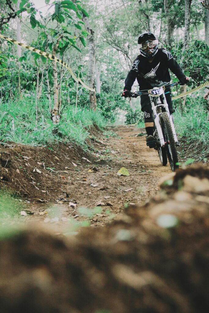 A biker rides fast down a forest trail, showcasing thrilling mountain biking action.